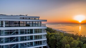 Un edificio moderno de varios pisos con grandes ventanales, una escalera de cristal y vista al atardecer sobre el océano.