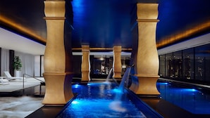 Un área de piscina interior moderna con un elemento central de agua y grandes columnas.