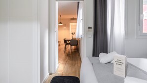 Une chambre d’hôtel comprenant un lit, une table de chevet, un petit bureau et une chaise. Une porte donne accès à un coin repas avec une table et des chaises.