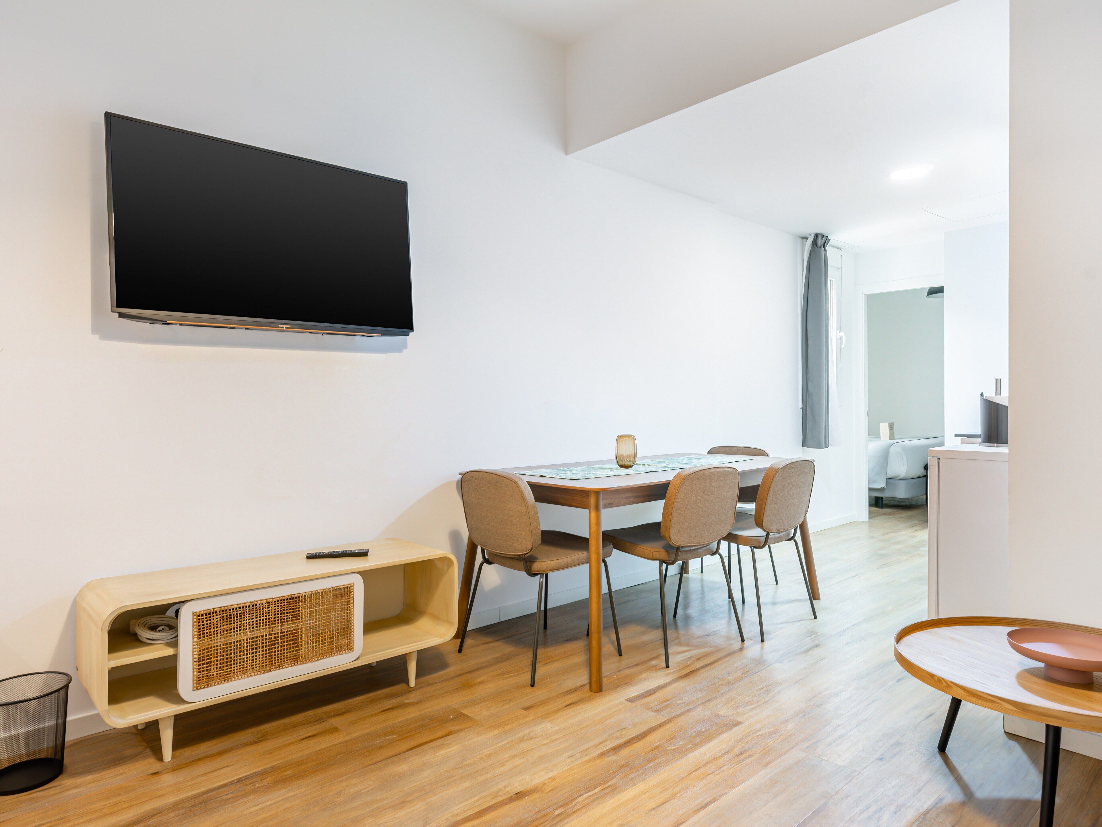 A modern dining area with a wooden table, four chairs, a television mounted on the wall, and a small cabinet with a woven basket.