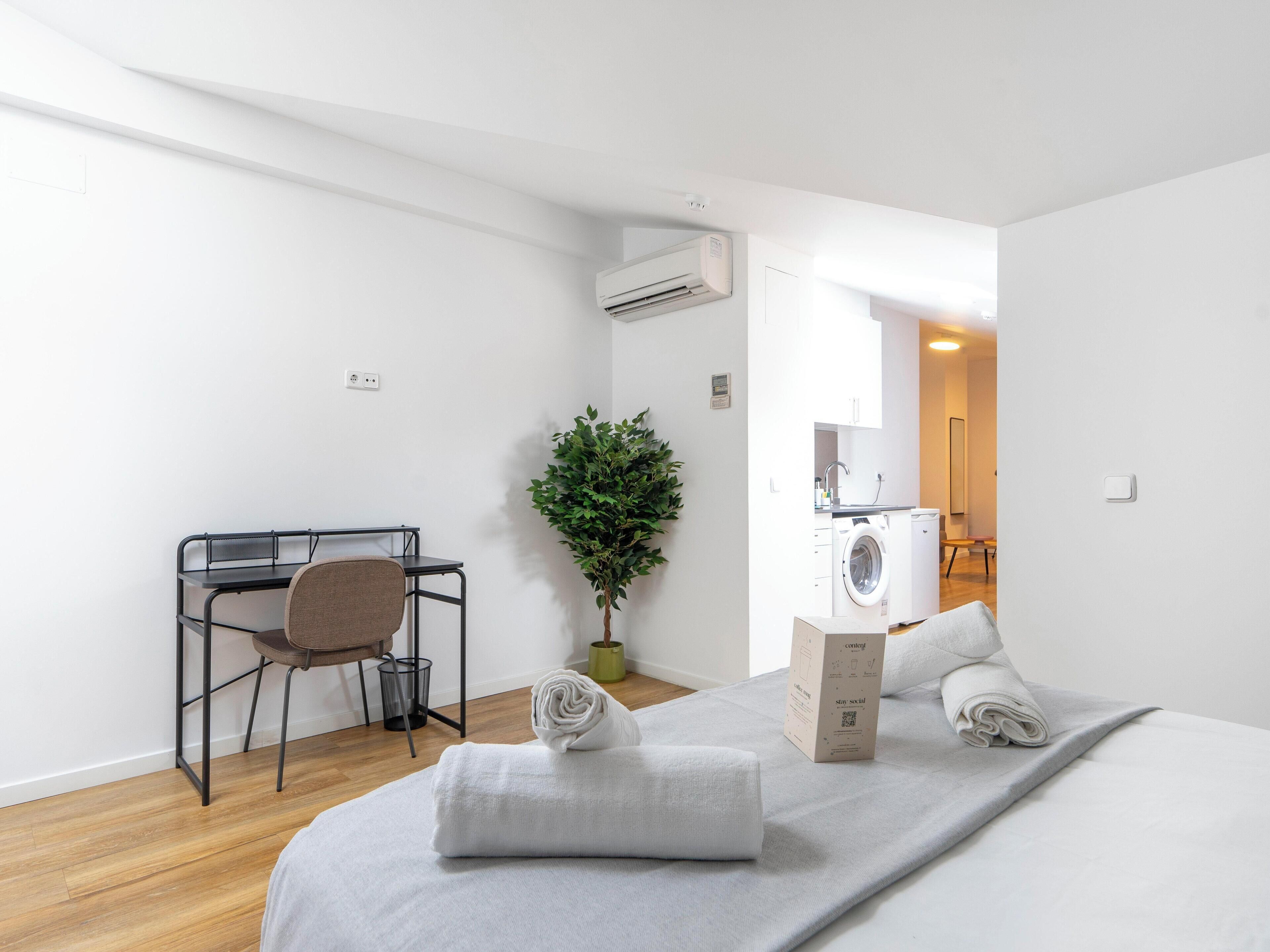 A modern, minimalist bedroom with a bed, a desk, and a washing machine.