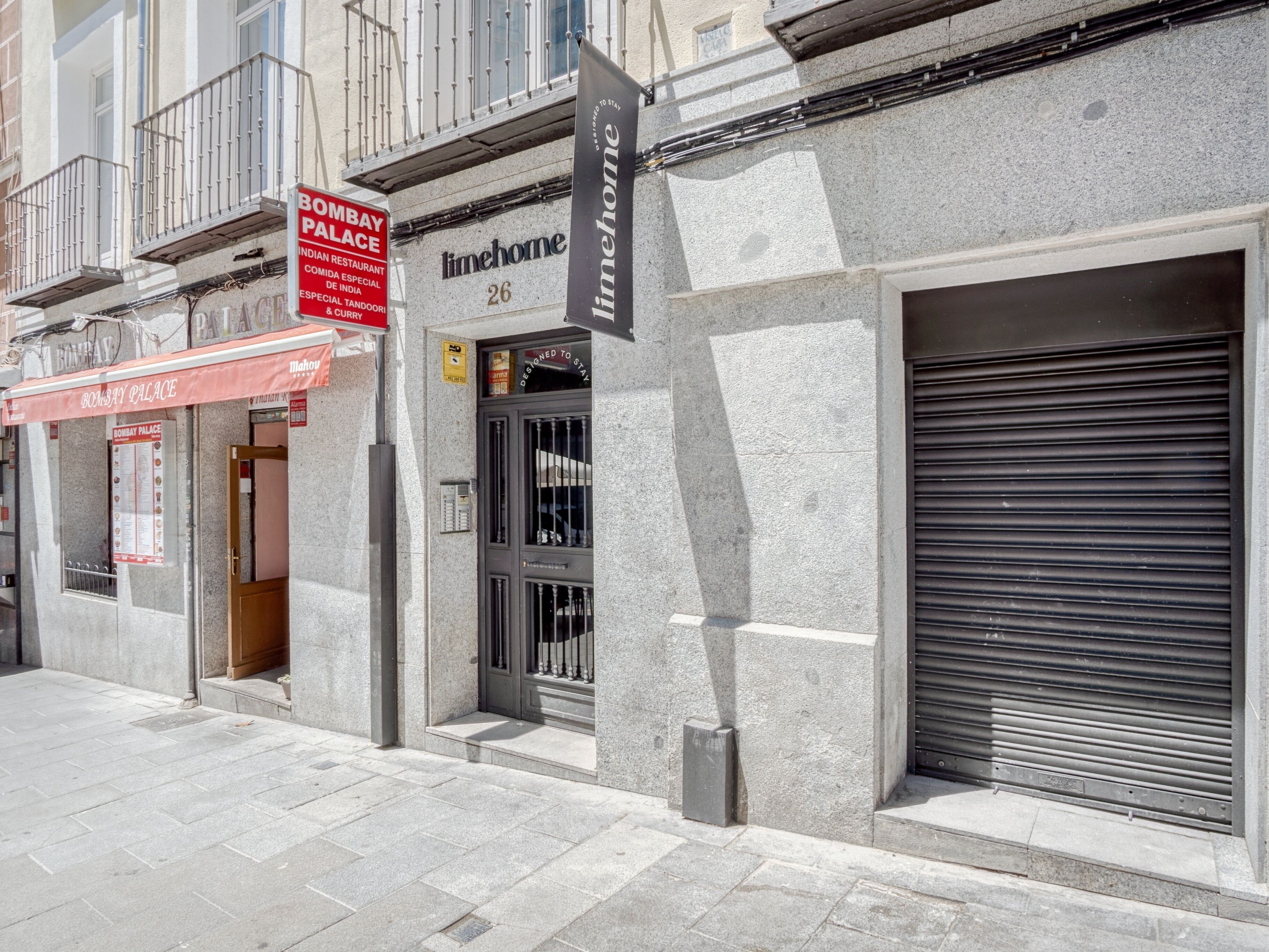 A building with a closed shutter, a sign for 'Bombay Palace' restaurant, and a 'limehome' sign.