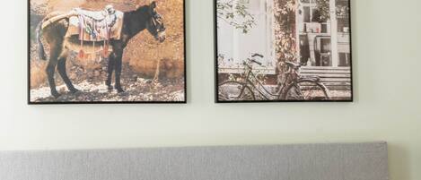 Deux tableaux encadrés sont accrochés au mur, au-dessus d’un lit agrémenté d’oreillers sur lesquels on peut lire les inscriptions « bonne matinée en suite » et « douces nuits en suite ».