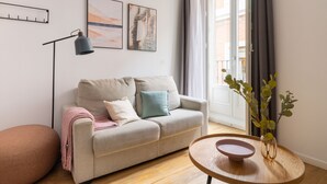 Un salon moderne avec un canapé, une table d’appoint, un lampadaire et une fenêtre avec des rideaux.