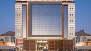 A hotel with a large sign reading "Roots Hotel" and Arabic text. It features a modern facade with large windows and a prominent entrance. - Roots Hotel (Makkah)