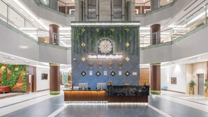 A hotel reception area with a modern design, featuring a central reception desk, multiple seating areas, and a decorative wall with a logo. - Roots Hotel (Makkah)