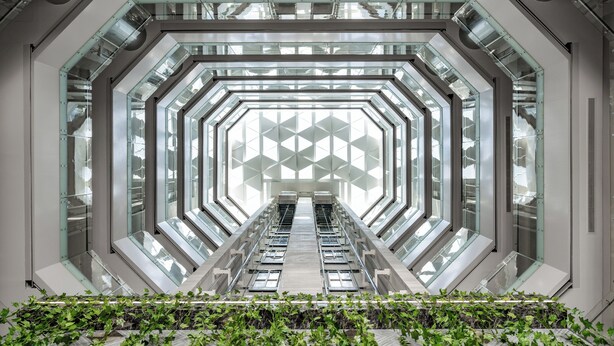A modern, geometric interior with a central escalator surrounded by glass walls and a geometric pattern on the ceiling. - Roots Hotel (Makkah)
