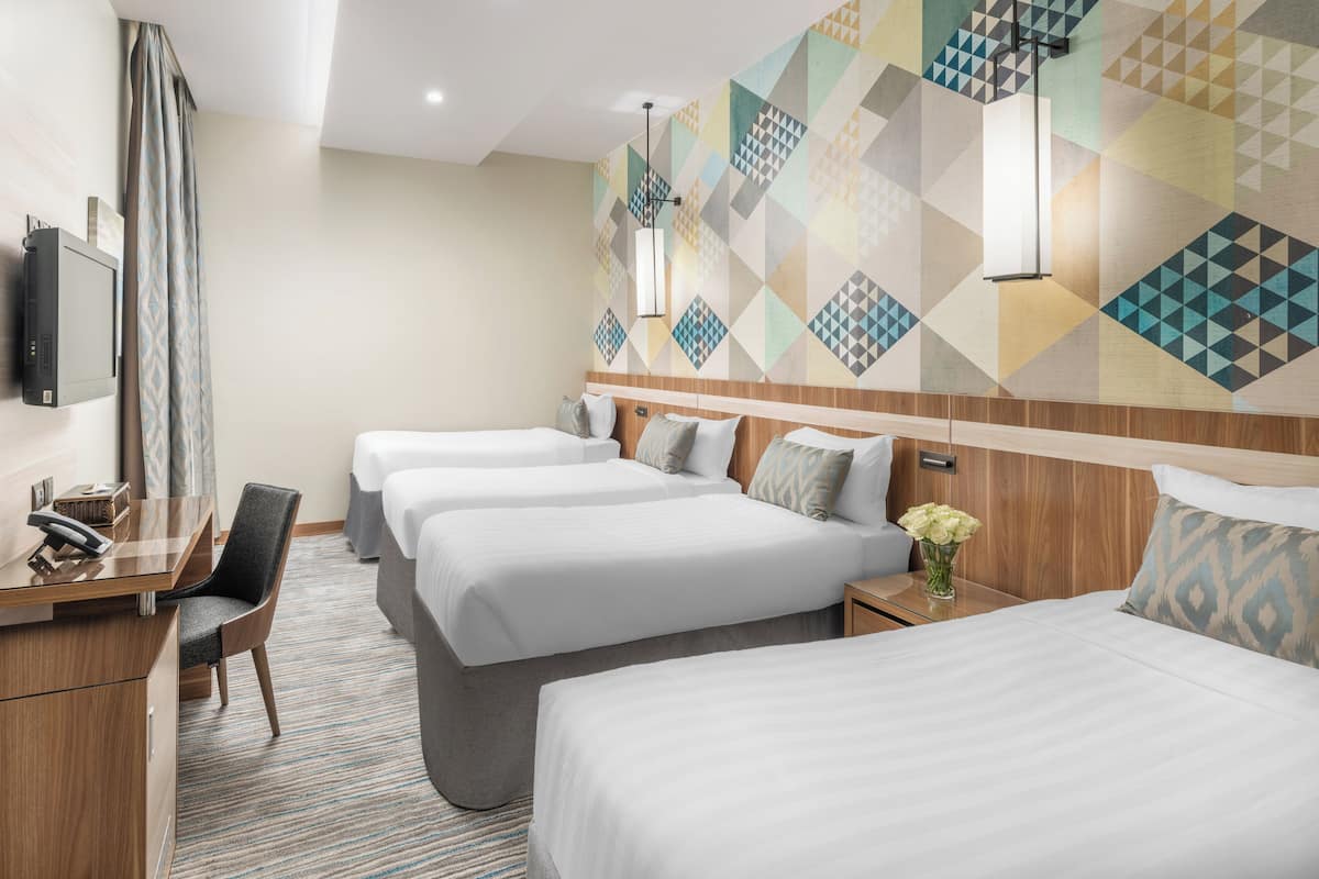 A hotel room with three beds, a desk with a chair, a TV, and a patterned wall.