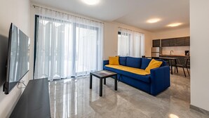 Ein modernes Wohnzimmer mit einem blauen Sofa, einem kleinen Couchtisch und einem an der Wand befestigten Fernseher.