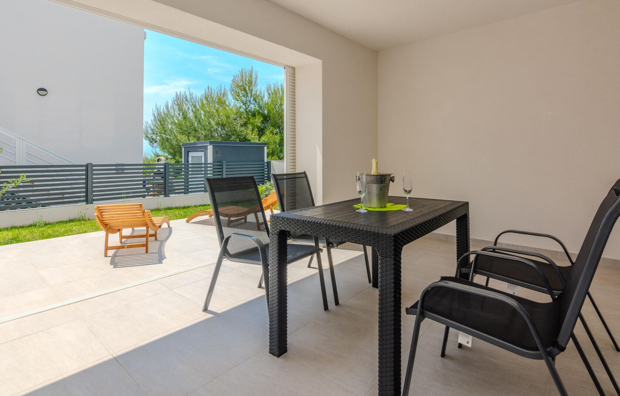 Une terrasse extérieure avec une table et des chaises, une petite construction en arrière-plan et une vue sur la verdure.