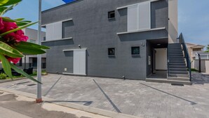 Ein modernes, zweistöckiges Gebäude mit einer grauen Fassade, zahlreichen Fenstern und einer sichtbaren Treppe zum Eingang.