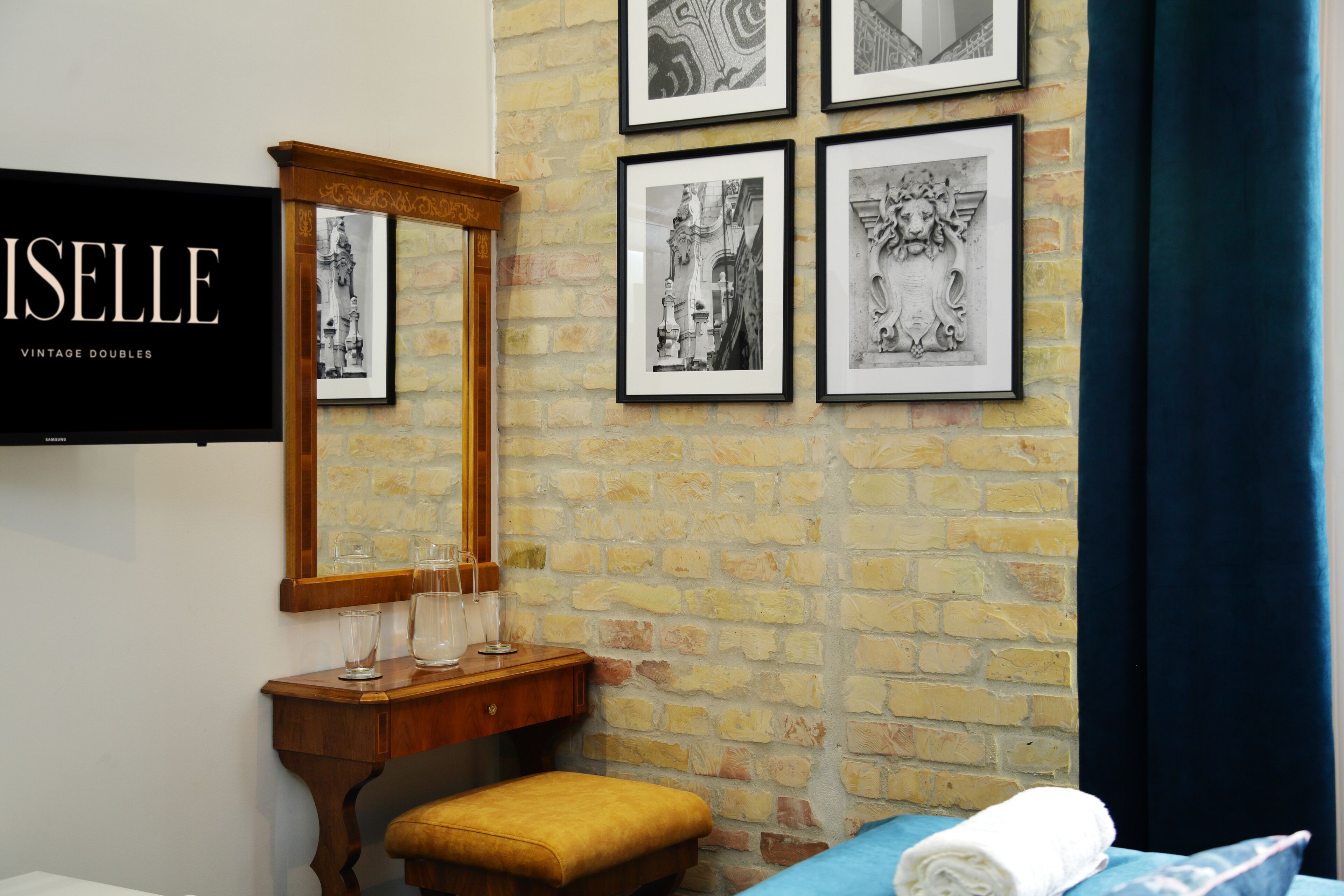 A hotel room with a brick wall, a wooden vanity with glasses, a mirror, and framed black and white artwork.