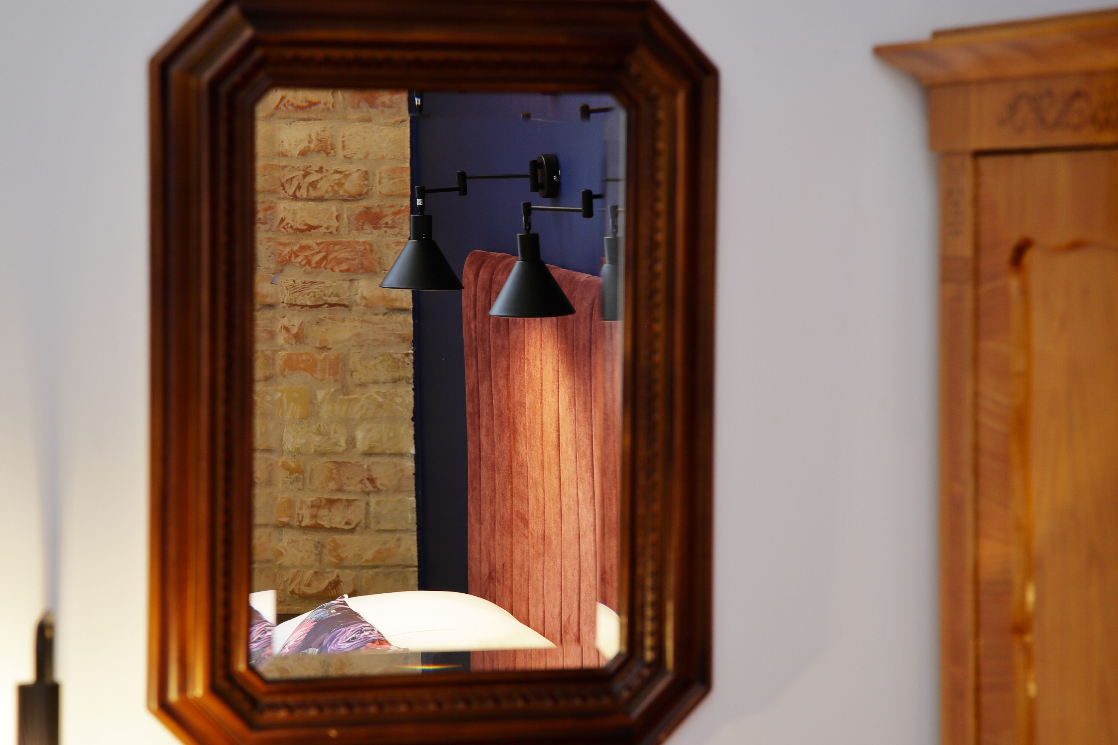 Un espejo refleja una habitación con pared de ladrillo, paneles de madera y dos lámparas colgantes negras.