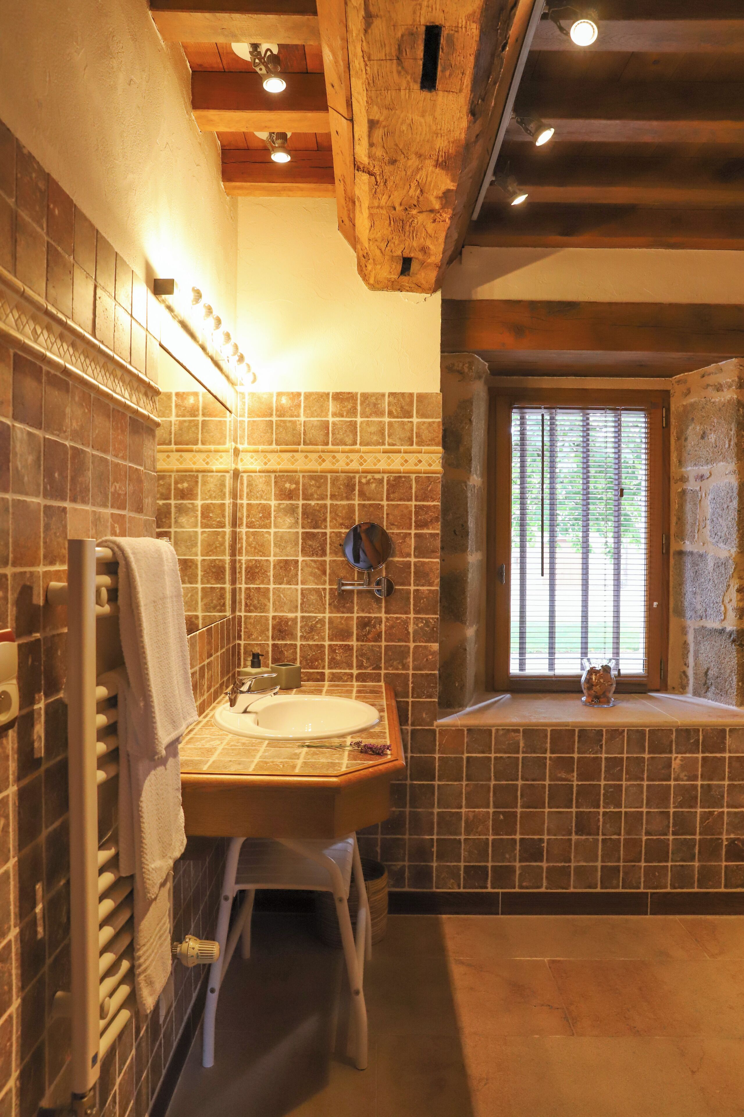 A bathroom with a wooden ceiling, a sink, a mirror, and a window with blinds.
