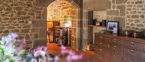 A stone-walled room with a wooden dresser, a bookshelf, and an arched doorway leading to another room.