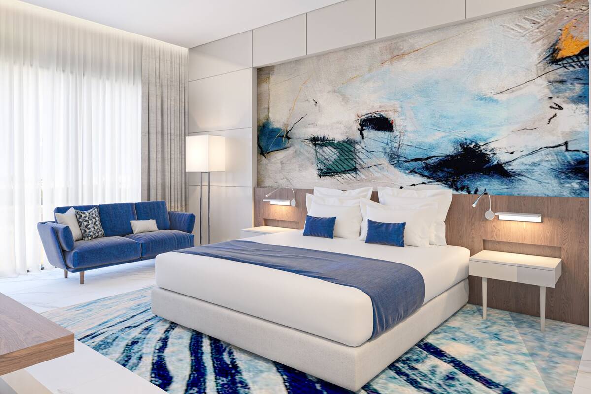 Een moderne hotelkamer met een groot bed, een blauwe bank en een groot abstract schilderij aan de muur.