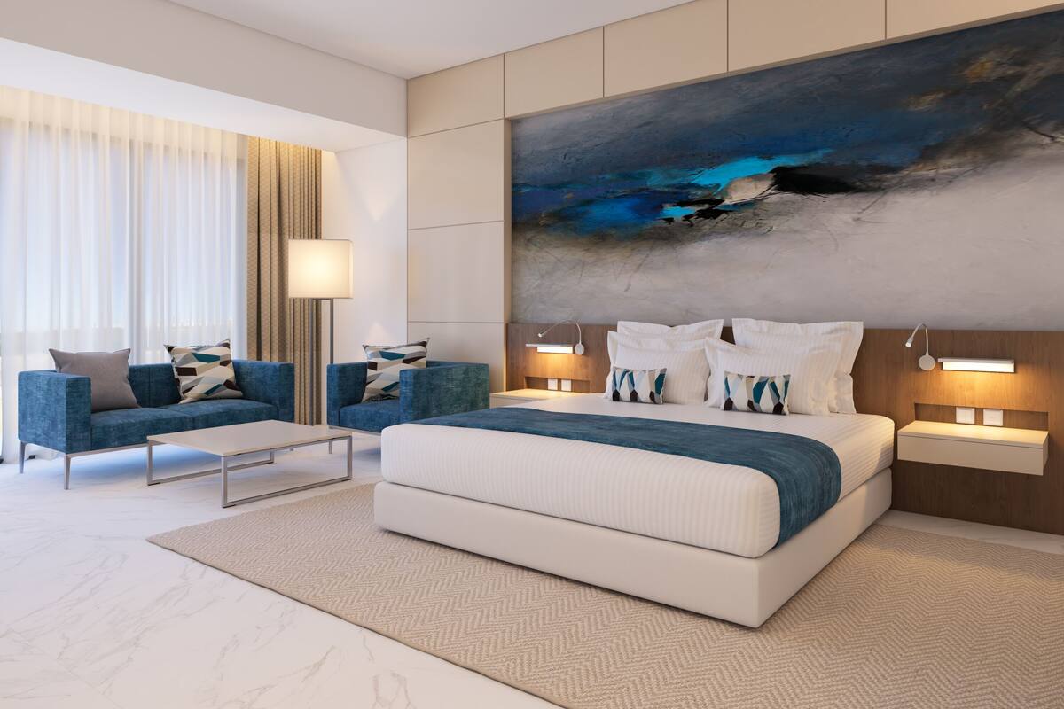 Een moderne hotelkamer met een groot bed, twee sofa's, een bijzettafeltje en een groot abstract schilderij aan de muur.