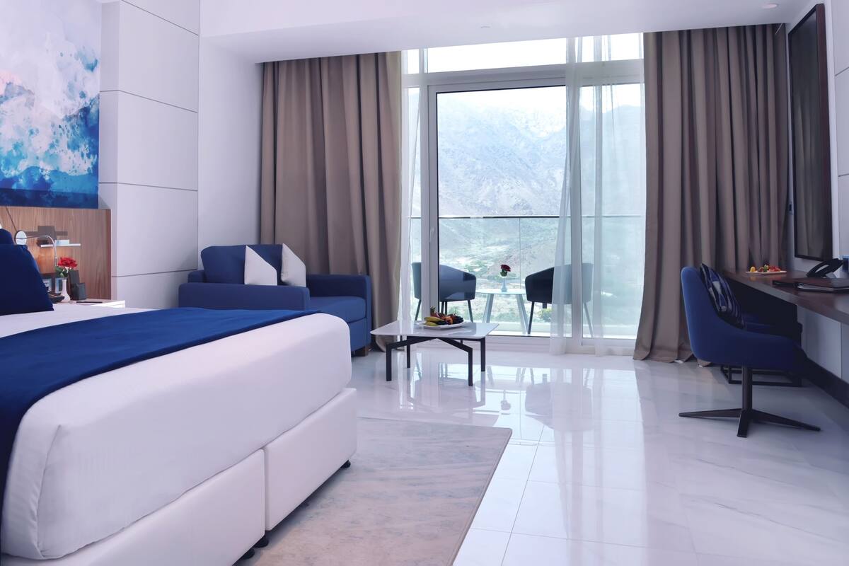 Een moderne hotelkamer met een groot bed, een bureau, een stoel en een balkon met uitzicht.