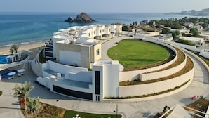 A modern hotel with a central courtyard, a pool area, and a view of the sea and a small island.