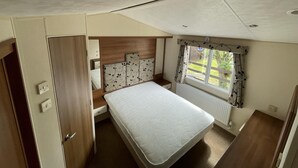 Une chambre à coucher de taille modeste, comprenant un lit, une tête de lit en bois, une fenêtre avec des rideaux et un radiateur.