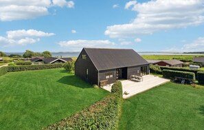 Une maison moderne dotée d’une grande terrasse, entourée de pelouses bien entretenues et offrant une vue sur un lac.