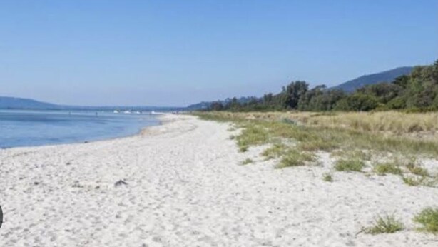 Une plage de sable, un ciel dégagé et des collines à l’horizon.