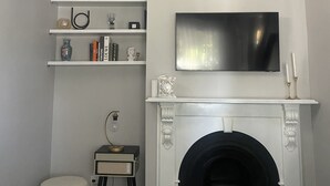Un salon doté d’une cheminée, d’un téléviseur fixé au mur et d’étagères où sont disposés des livres et des objets décoratifs.