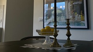 Une table à manger sur laquelle se trouve un saladier en verre rempli de citrons et un chandelier. Deux photographies encadrées sont accrochées au mur, au-dessus de la table.