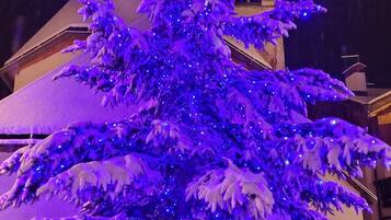 A snow-covered Christmas tree with blue lights in front of a church with a clock tower.