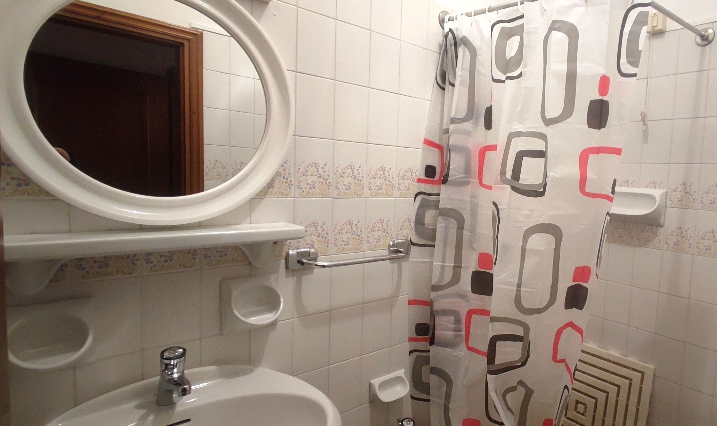 A bathroom with a white sink, a mirror, a toilet, and a shower curtain with geometric patterns.
