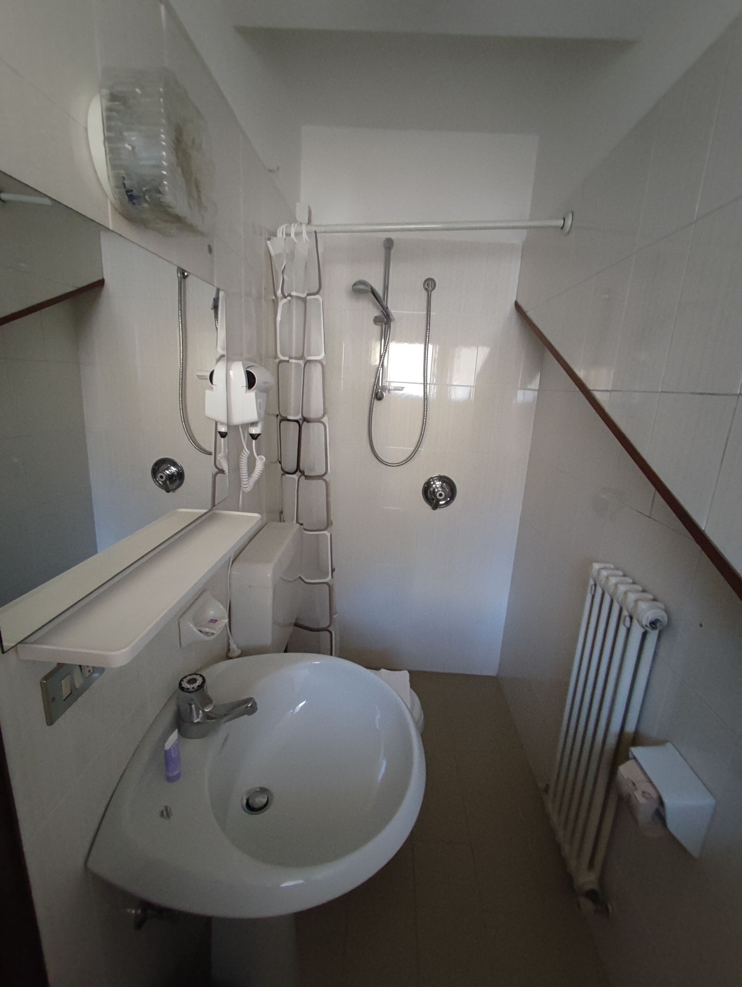A small, modern bathroom with a white sink, a mirror, a shower, and a toilet.