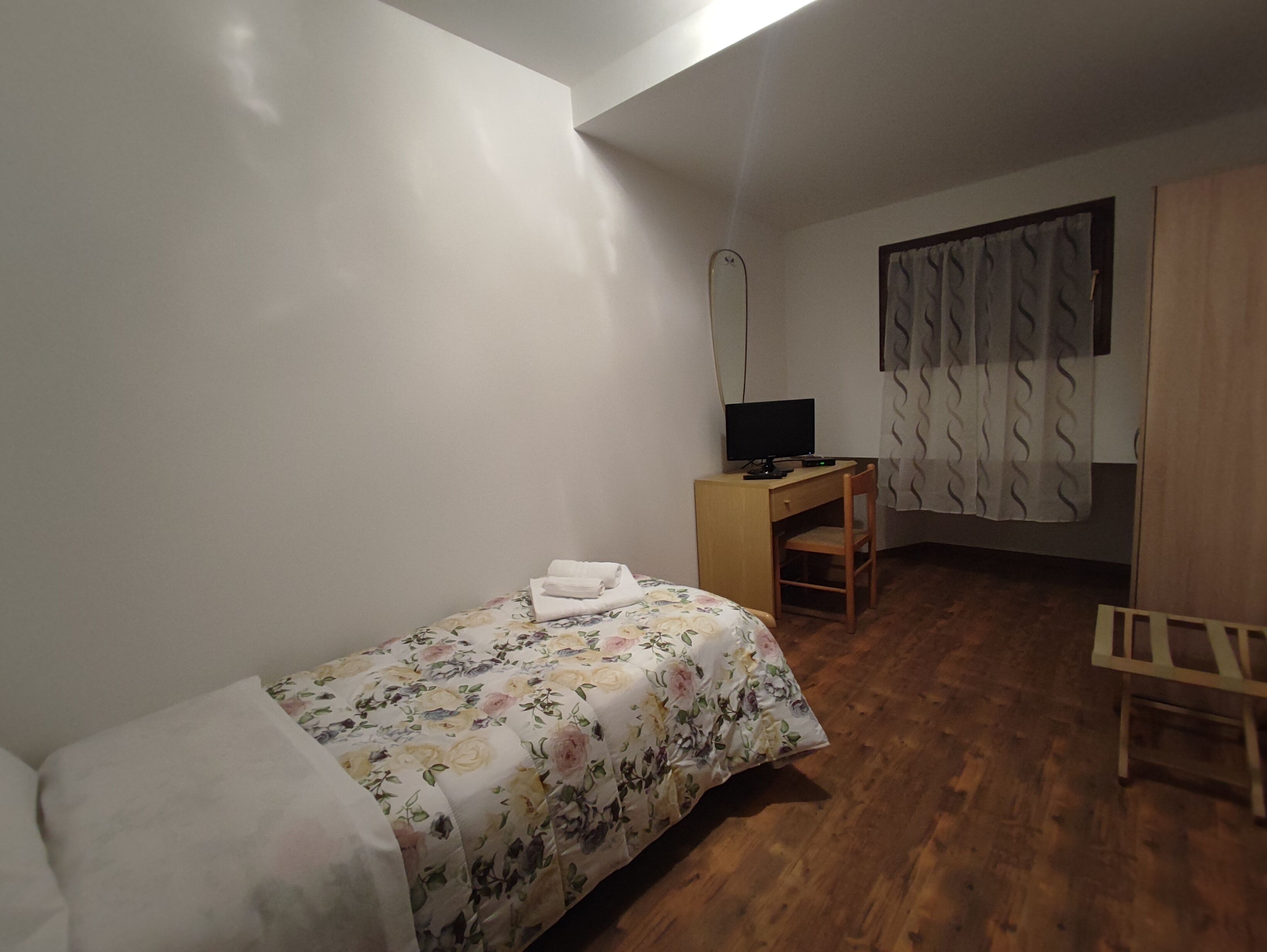 Une petite pièce, peu meublée, avec un lit simple, un bureau et une chaise.