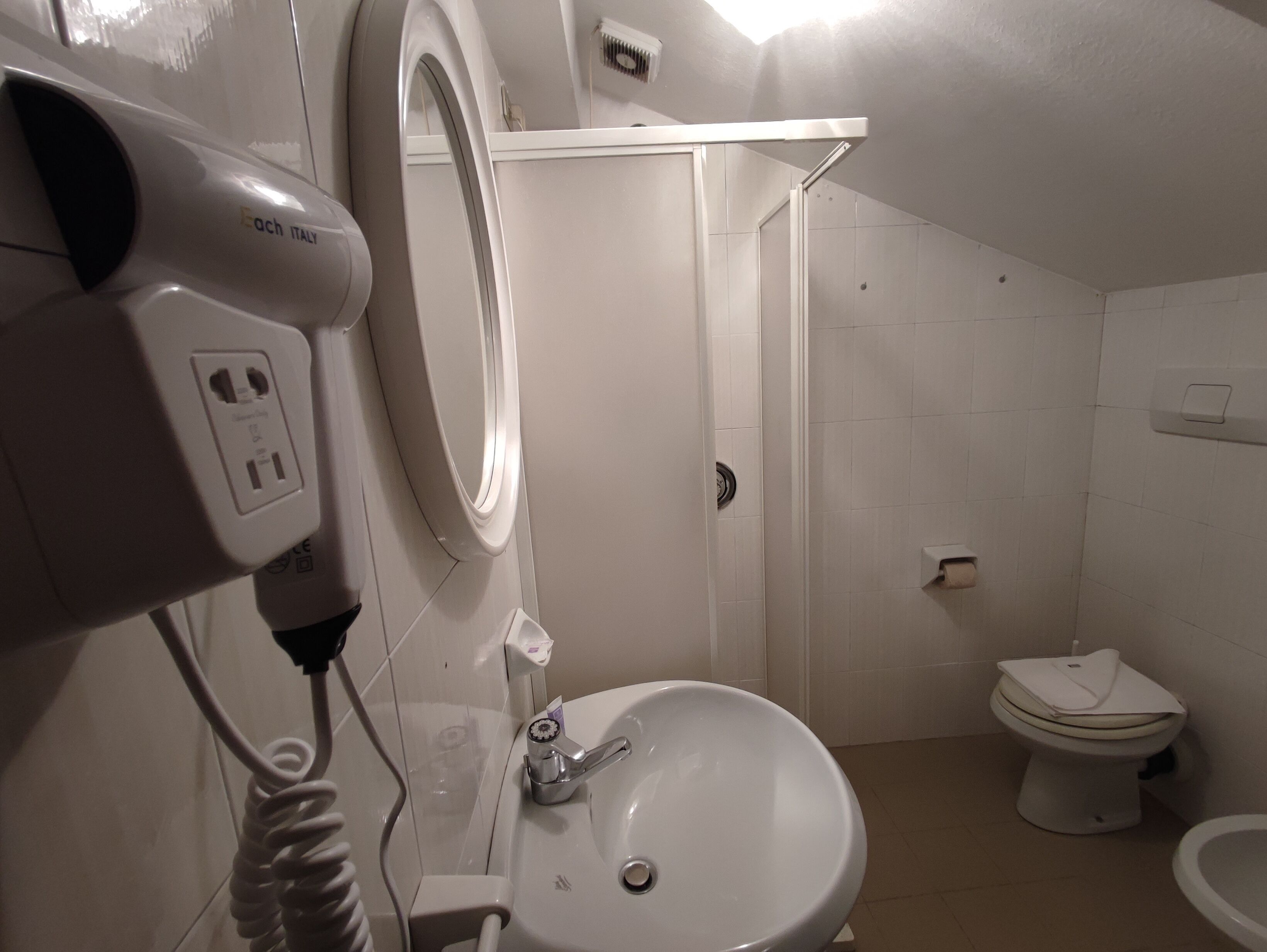 A bathroom with a sink, toilet, and a hairdryer plugged in.