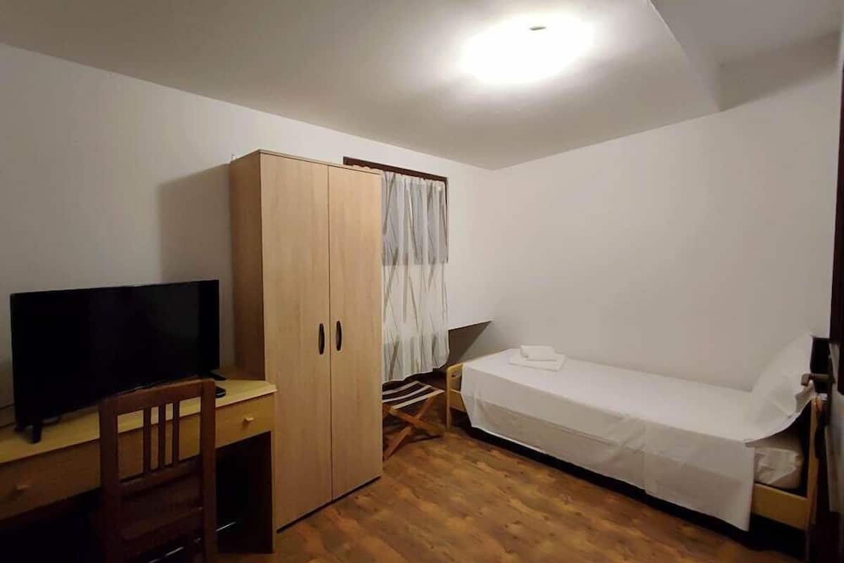 A bedroom with a bed, a desk with a television, a wardrobe, and a window with curtains.