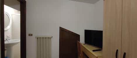 Et lille værelse med et træskrivebord, et fjernsyn, en radiator og et klædeskab.