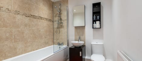 Un baño moderno con bañera, ducha con mampara de vidrio, lavabo blanco y retrete.