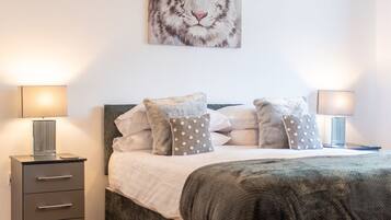 Une chambre à coucher comprenant un lit, deux tables de chevet, une lampe, une commode et une œuvre d’art représentant un tigre, accrochée au mur.