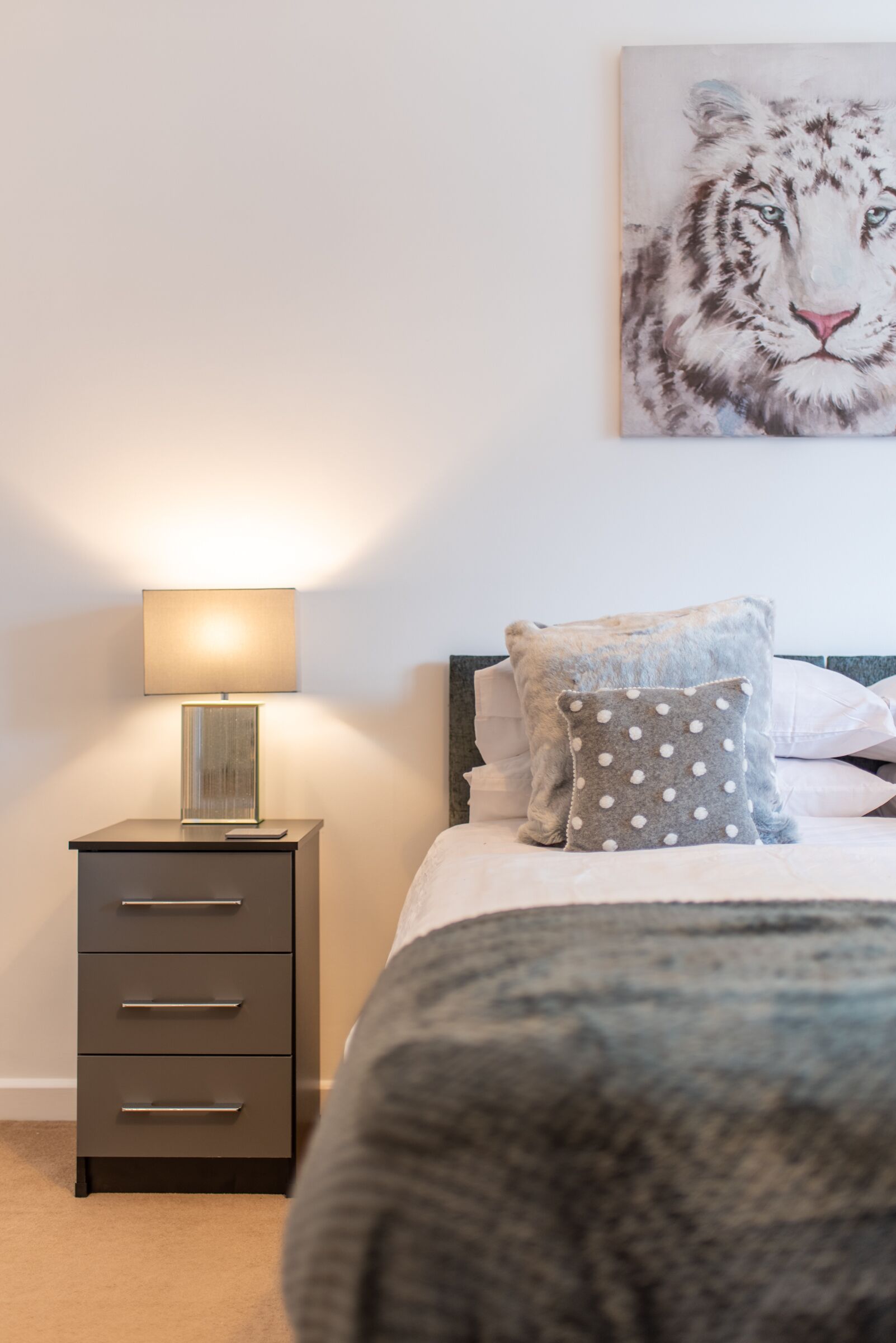 Un dormitorio con una cama, una mesita de noche con lámpara, una cómoda y un cuadro de un tigre en la pared.