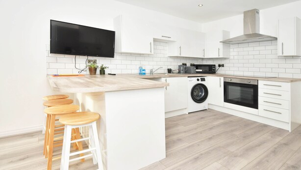 A modern kitchen with white cabinetry, a wooden countertop, a washing machine, and a built-in oven. - Townhouse@ 147 Westminster Street Crewe (Crewe)