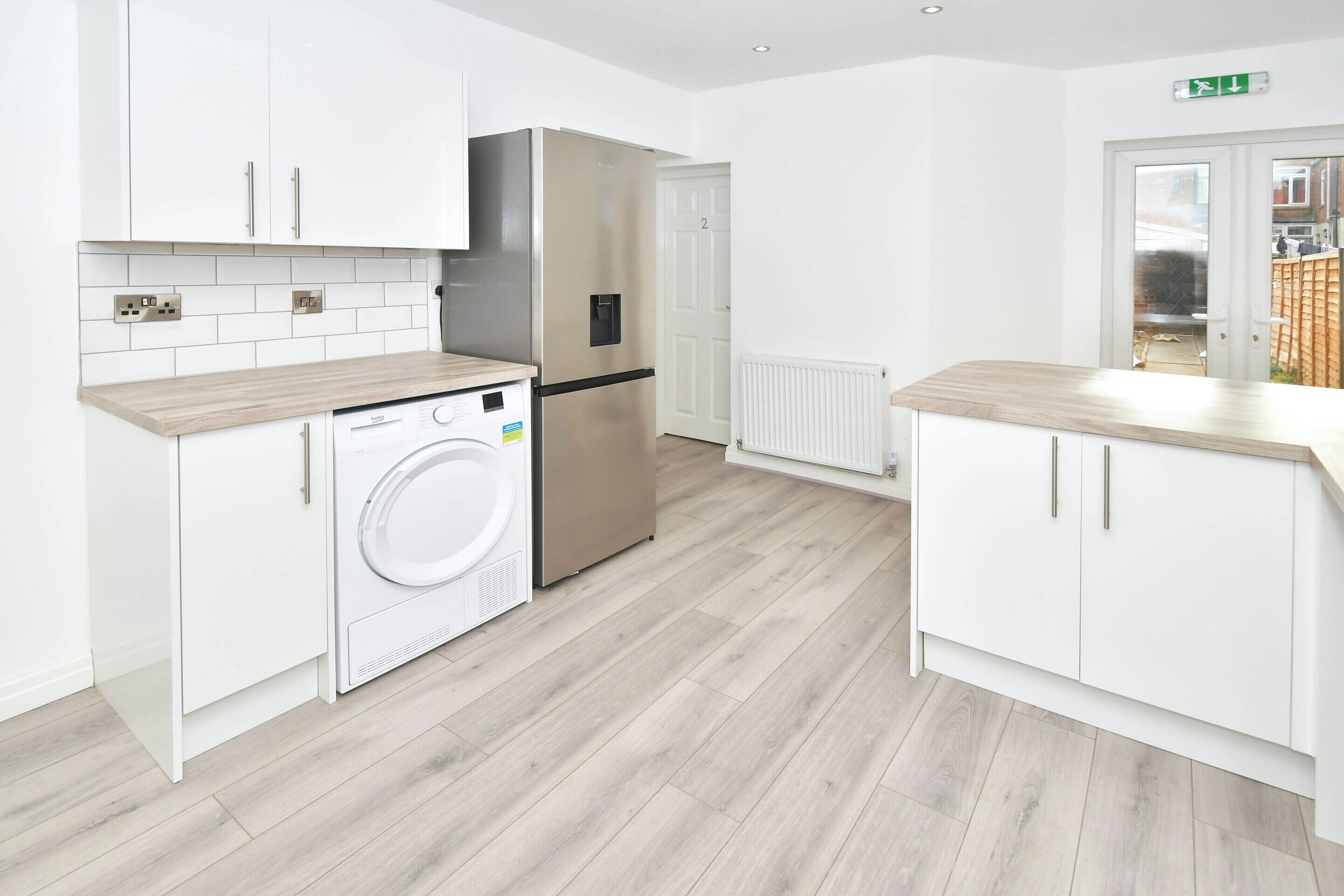 Eine moderne Küche mit weißen Schränken, einem Edelstahl-Kühlschrank, einer integrierten Waschmaschine und einer Holz Arbeitsplatte.
