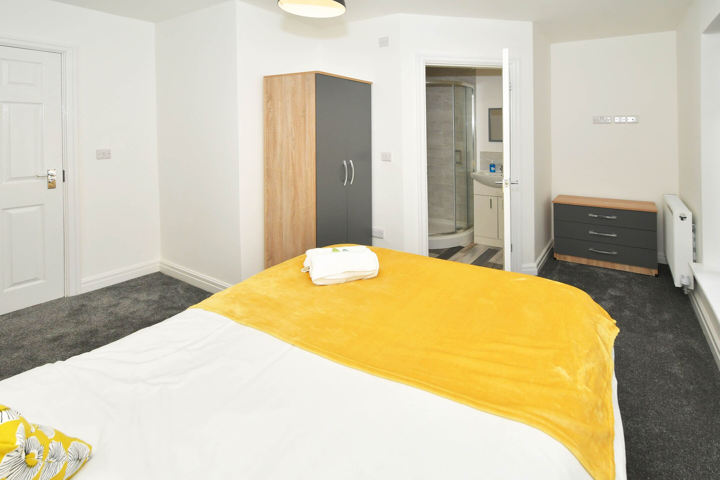 A hotel room with a bed, a wardrobe, a bathroom with a shower, and a small desk.