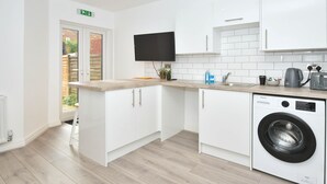 A modern kitchen with white cabinets, a built-in washing machine, a flat-screen TV, and a wooden countertop. - Townhouse@ 147 Westminster Street Crewe (Crewe)
