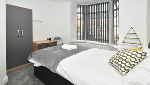 A bedroom with a bed, a wardrobe, a bedside table, a lamp, and a window with blinds. - Townhouse@ 147 Westminster Street Crewe (Crewe)