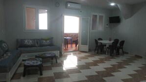 A living room with a sofa, a small table, and a dining area with chairs. There is a door leading to an outdoor area. - Appartment F1 Bab El-assa (souk tlata)