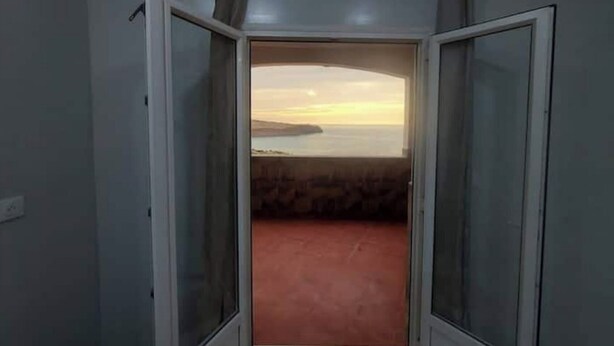 A room with a view of a sunset over water, a red carpet, and a door leading to another room. - Appartment F1 Bab El-assa (souk tlata)