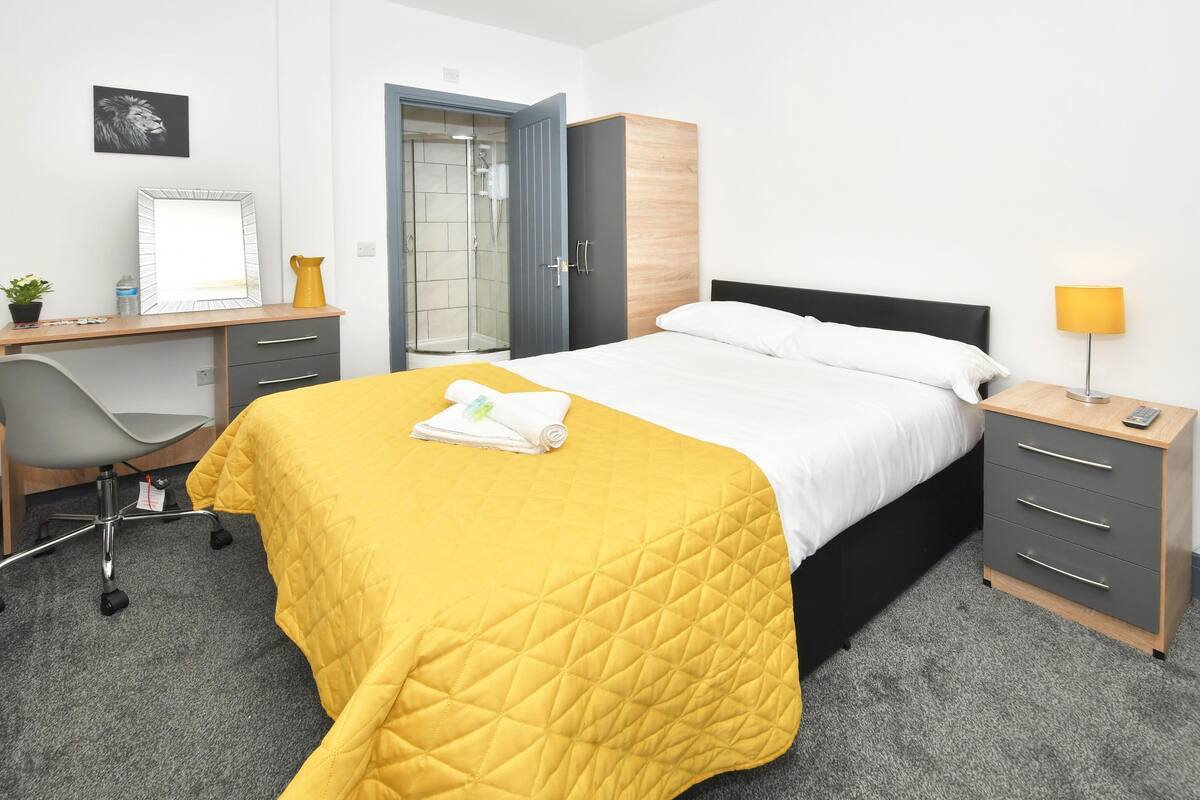 Une chambre d’hôtel comprenant un lit, un bureau, une chaise, une armoire et une table de chevet avec une lampe.