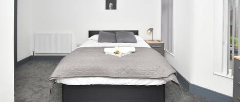 A neatly arranged bedroom with a bed, bedside table, lamp, and a framed picture on the wall.