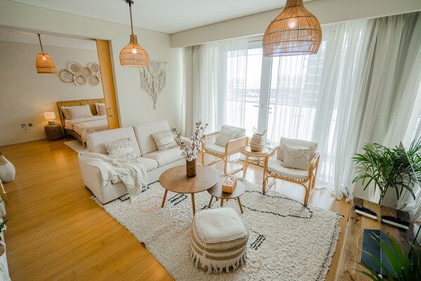 A modern living room with a sofa, armchairs, a coffee table, and a rug. There are hanging lights and a plant.