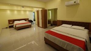 Una habitación de hotel con dos camas, una colcha roja y blanca, un ventilador de techo y un aire acondicionado.
