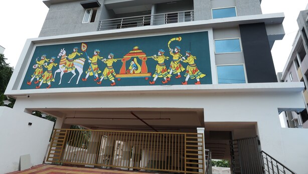 Un edificio de varios pisos con un diseño arquitectónico moderno, que presenta un gran mural en la fachada que representa una escena tradicional.
